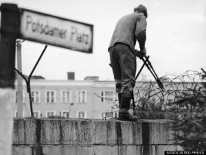 At Potsdam square, an East German army soldier snips away at barbed wire atop the wall dividing Berlin, Germany on August 12, 1966. The communist are tearing down the old wall and building a new one. The barrier will be five years old. (AP Photo/Herrmann)